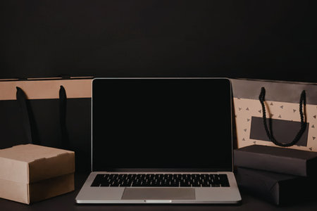 A laptop with a black screen is surrounded by shopping bags and boxes on a table.の写真素材