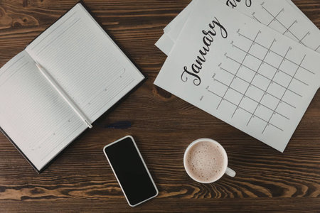 A flat lay of a morning routine setup on a wooden desk with a notebook, calendar, smartphone, and a...