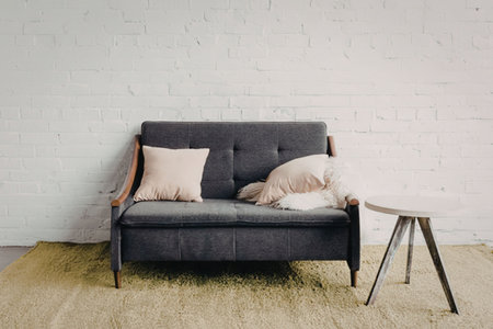 A modern living room setup featuring a dark gray sofa with beige pillows and a small wooden table on...