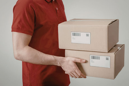 A man in a red shirt holding two brown packages with barcode labels