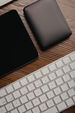 A modern workspace featuring a tablet, a portable hard drive, and a keyboard on a wooden desk.