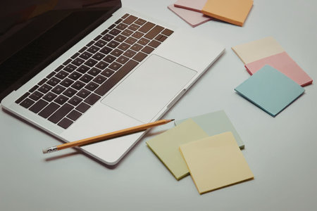 A laptop with a pencil on top, surrounded by colorful sticky notes on a desk.