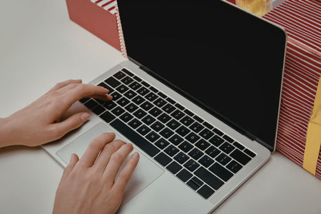 A person typing on a laptop with a blank screen, surrounded by colorful boxes on a white table.
