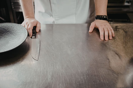 a man in a white shirt standing behind a stainless steel surface with a plate and knife
