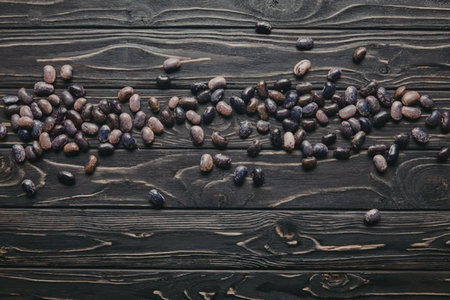 A collection of small, purple and brown seeds scattered on a dark wooden surface.