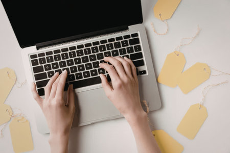 A person typing on a laptop keyboard surrounded by yellow tags on a white surface