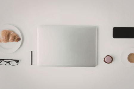 A minimalist workspace setup featuring a laptop, coffee, and a croissant on a clean white desk.