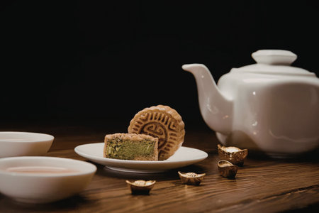 A serene setting featuring a white teapot, a plate with a mooncake and a slice of mooncake, and...