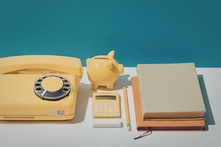 A yellow telephone, piggy bank, calculator, pencil, and notebooks on a desk.の写真素材