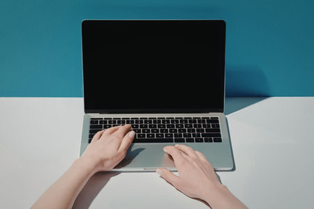 A person typing on a laptop with a blank screen on a white table against a blue background.