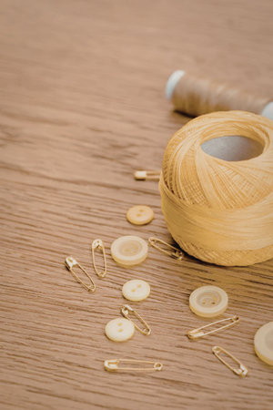A spool of yellow thread with buttons and pins on a wooden surface