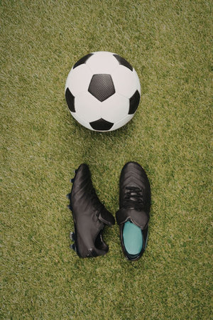 A soccer ball and a pair of black cleats on a green grass field