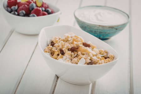 Bowl of muesli with dried fruit and nuts served on a white wooden table accompanied by a bowl of...