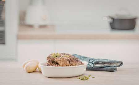 Roasted chicken and potatoes served in a white bowl on a kitchen counter with a blue towel and fresh...