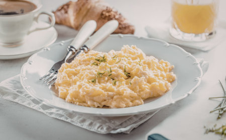 Scrambled eggs are served on a white plate with a croissant, coffee, and orange juice on a white tablecloth, creating a nutritious and delicious breakfast meal setting.の写真素材