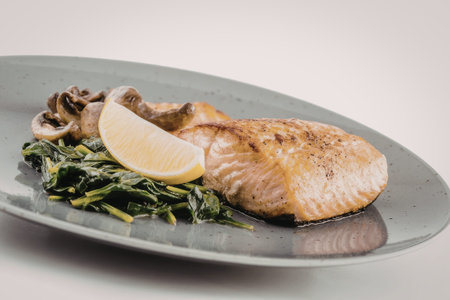 Grilled salmon fillet seasoned to perfection served alongside sautÃ©ed spinach and mushrooms on a...