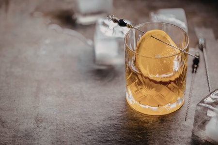 Crystal glass filled with amber liquid and garnished with an orange slice rests on a textured gray...