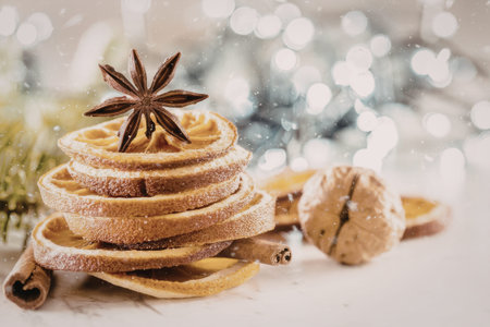 Dried orange slices are stacked with star anise and cinnamon on a marble surface surrounded by festive bokeh lights and holiday decorations, creating a cozy winter atmosphere.の写真素材