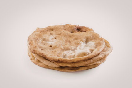 Stack of freshly baked golden brown pita bread placed on a plain white background symbolizing...