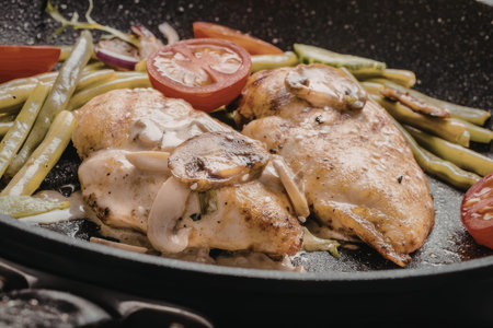 Grilled chicken breast and mushrooms are cooked with green beans and tomatoes in a black skillet,...