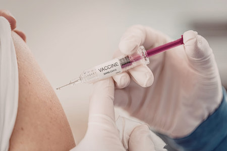 Close-up of a medical professional in gloves administering a COVID vaccine using a syringe,...