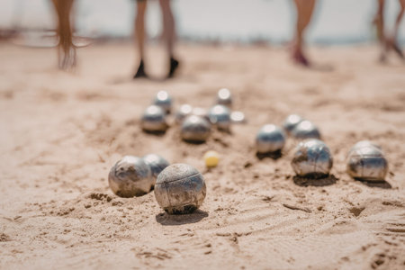 People play boules or petanque on a sandy beach with metal balls scattered around a small yellow...