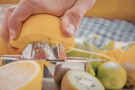 Person squeezes orange into a manual citrus squeezer surrounded by various fruits like lemon, kiwi,...