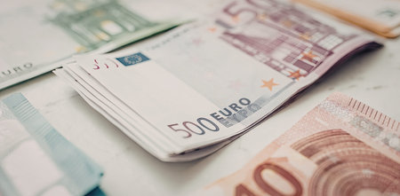 Stack of 500 euro banknotes lies on a surface surrounded by other euro denominations, symbolizing...