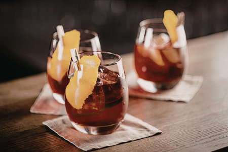 Three stemless glasses filled with red sangria are garnished with orange slices and straws on a...