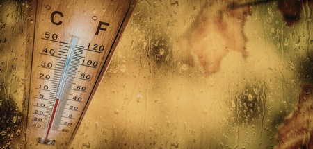 Wooden thermometer displays temperature on a rainy day with water droplets on the surrounding glass...