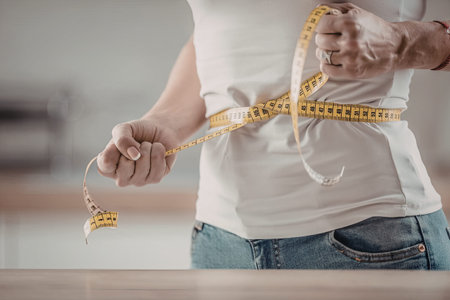 Woman measures her waist with a yellow tape measure indicating progress in weight loss and fitness...
