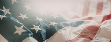 American flag waving gently with sunlight shining down on its red white and blue colors symbolizing...