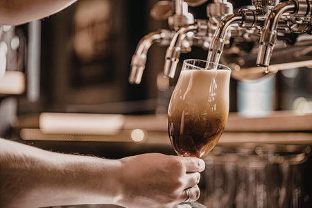 Bartender pours a rich amber beer into a glass from a row of shiny taps in a bustling bar...