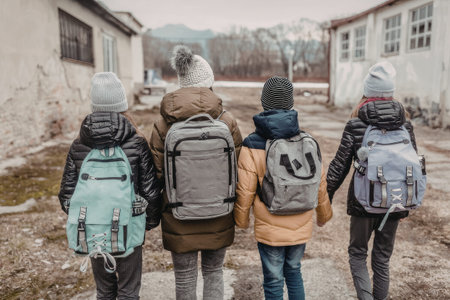 Four young children holding hands and walking to school with backpacks on a winter day near old...