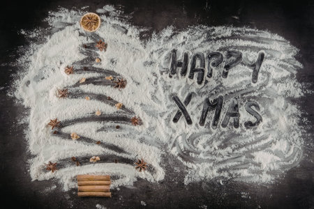 Christmas tree made from flour decorated with cinnamon sticks and star anise on a dark background with the words happy xmas.の写真素材