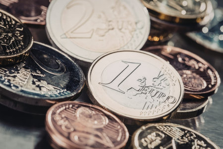 Euro coins of various denominations and colors are scattered on a metallic surface, creating a...