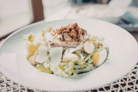 Grilled chicken salad with croutons and boiled eggs served on a white plate, displayed nicely on a woven placemat on a table.の写真素材