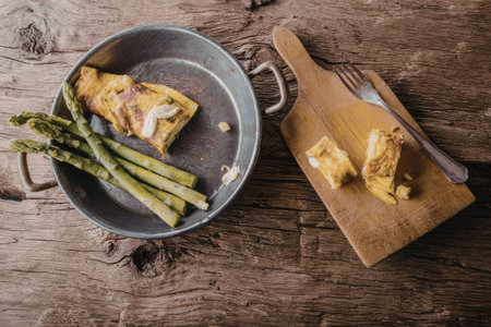 Delicious omelette served with steamed asparagus on a rustic wooden table setting for a cozy breakfast or brunch meal.の写真素材