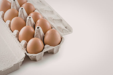 Dozen fresh brown eggs are neatly arranged in a cardboard container, showcasing their natural...