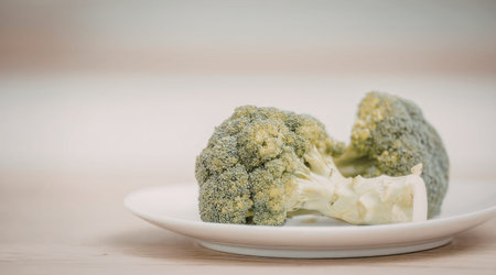 Fresh broccoli florets are carefully arranged on a white plate ready to be consumed or used in a...