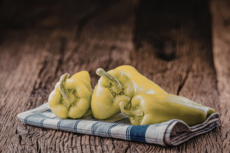Yellow bell peppers arranged on a blue and white stripped kitchen towel placed on a rustic wooden...