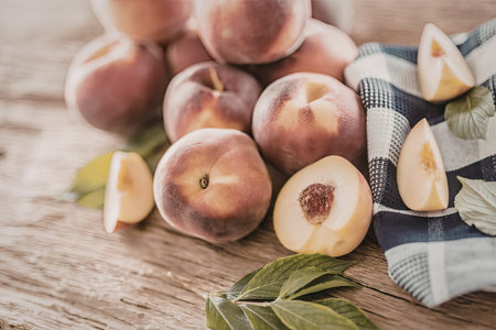 Fresh ripe peaches arranged on a wooden surface with a blue and white striped towel and green leaves...