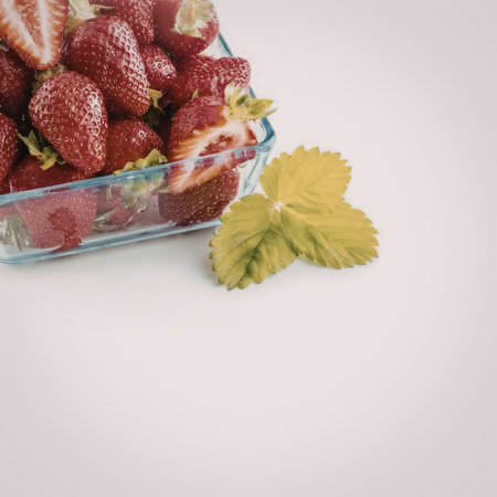 Fresh ripe strawberries in a clear plastic container with green leaves on a white background...