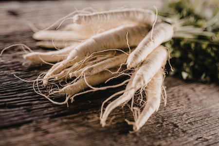 Fresh horseradish roots rest on a rustic wooden table surrounded by green leaves showcasing their...