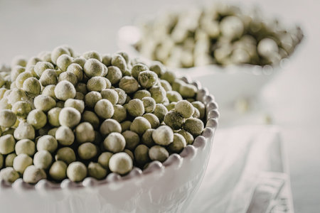 Frozen green peas overflowing from a white bowl on a clean white surface ready for cooking and preparation.の写真素材