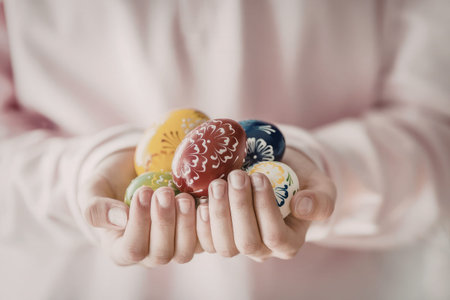 Person gently holds colorful decorated Easter eggs in their cupped hands against a blurred pink background symbolizing spring celebration and festive tradition.の写真素材