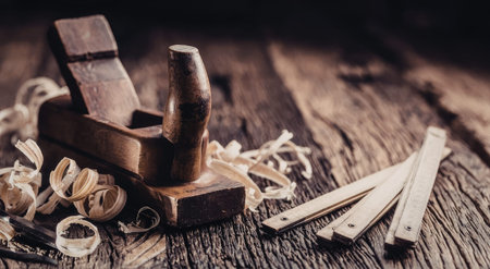 Woodworking tools including a wooden hand plane and metal chisels lie on a wooden surface surrounded...