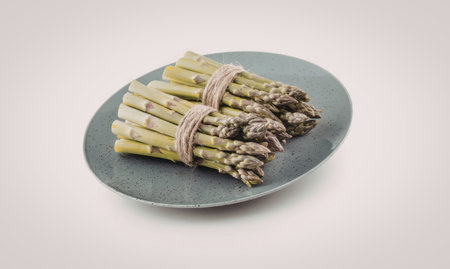 Fresh green asparagus spears tied together with twine on a plate, ready to be cooked or served as a nutritious and delicious meal.の写真素材