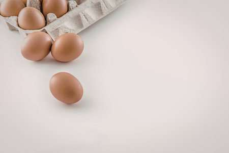 Brown eggs in a carton with one egg outside on a white surface for cooking and baking needs.