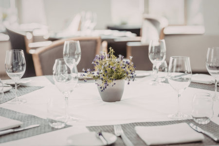 Elegant dining table set with wine glasses, cutlery, and a small purple flower centerpiece in a...
